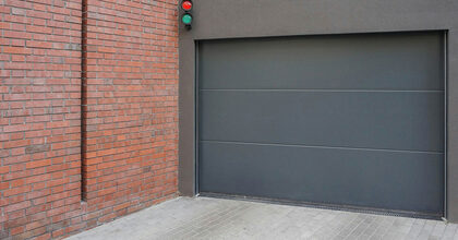 Puerta seccional de garaje gris junto a una pared de ladrillo con semáforo de acceso