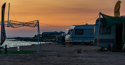 Caravanas aparcadas junto al mar al atardecer, con un toldo verde y una carpa plegable en primer plano