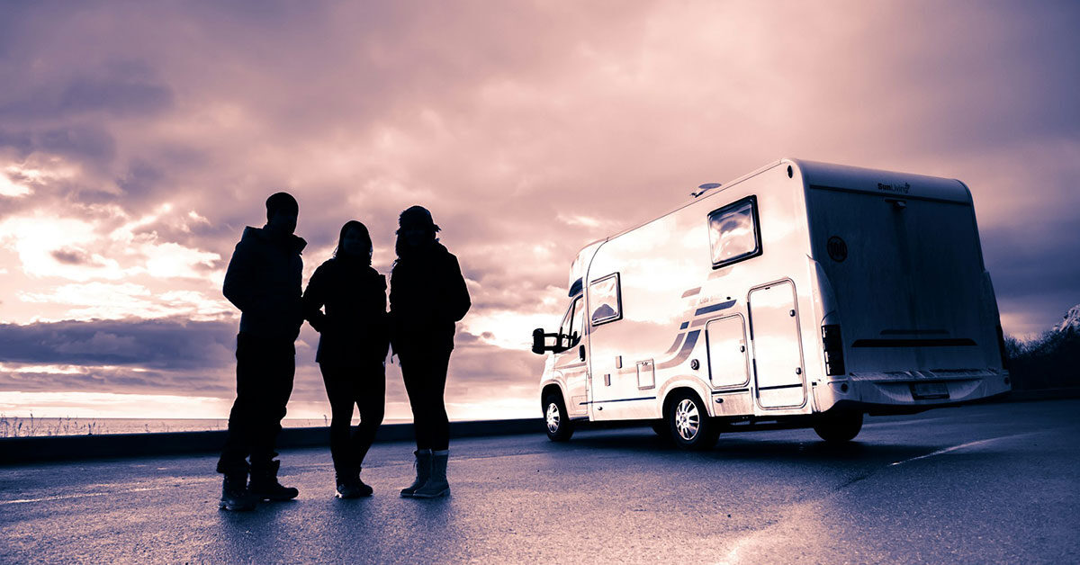 Tres viajeros junto a una autocaravana al atardecer en la costa